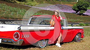 Happy woman in red dress enjoy sunset near classic vintage sports car