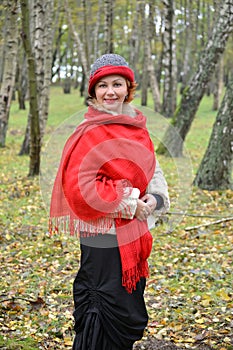 The happy woman in a red stole and a hat costs among birches in the wood