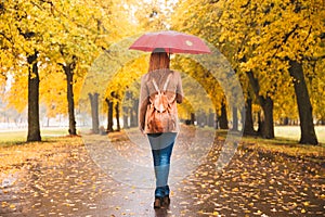 Happy woman with red umbrella walking at the rain in beautiful autumn park