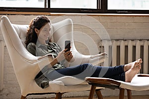 Happy woman relax in chair using modern smartphone