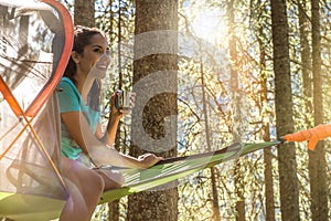 Happy woman relaxing in hanging tent camping in forest woods during sunny day.Group of friends people summer adventure