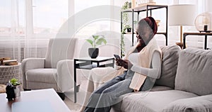 Happy woman relaxing on sofa while chatting using mobile phone