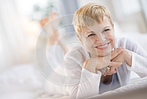 Happy Woman Resting Chin On Hands While Lying In Bed