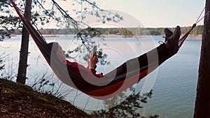 Happy woman, resting lying in hammock browsing in smartphone admiring lake.