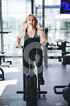 Happy woman riding an air bike at the gym.