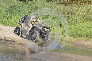 A happy woman riding a quad bike on the river.A girl on a Quad bike riding on the beach