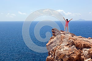 Happy woman on the rock with hands up. Winner, success, travel.