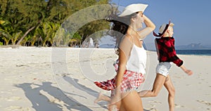 Happy woman running to water on beach, young girls throwing hats happy laughing