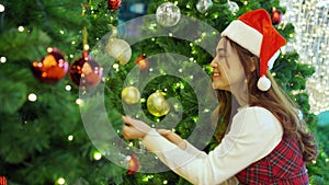 Happy woman in santa cap decorating Christmas tree