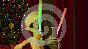 Happy woman in Santa costume plays with neon tubes near the tesla coil, against the background of the Christmas