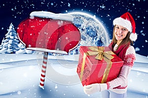 Happy woman in santa hat holding her big gift box against digitally generated christmas background