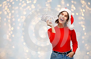 Happy woman in santa hat with money on christmas