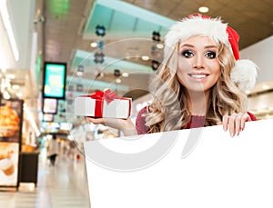 Happy woman Santa showing gift and white empty paper signboard