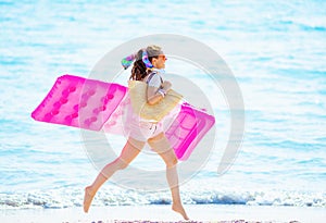 Happy woman on seacoast holding inflatable mattress and running