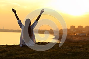Happy woman seeing city at sunset and raising arms photo
