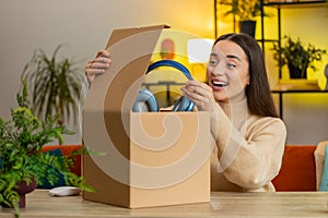 Happy woman shopper unpacking cardboard box delivery parcel online shopping purchase headphones