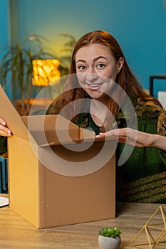 Happy woman shopper unpacking cardboard box delivery parcel online shopping purchase at home office