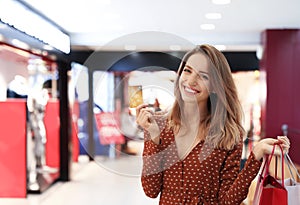 Happy woman with shopping bags and credit card in mall