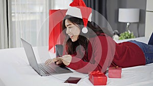 Happy woman shopping online for Christmas gift with computer laptop and credit card on bed