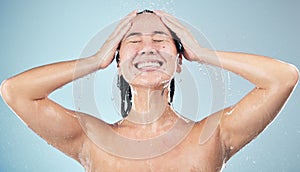 Happy woman, shower and water drops in hygiene, washing or grooming against a blue studio background. Female person