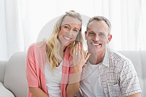 Happy woman showing engagement ring besides man