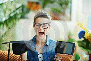 Happy woman showing graduation cap and tablet PC and rejoicing