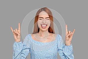 Happy woman showing her tongue and rock gesture on gray background