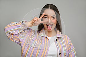 Happy woman showing her tongue and V-sign on gray background