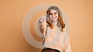 Happy woman showing thumbs up in brown studio