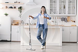 Happy woman showing thumbs up cleaning floor with spray mop