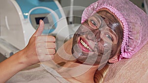 Happy woman showing thumbs up while having black mask on her face