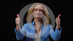 Happy woman showing thumbs up posing in camera flashes at black background. Portrait of smiling confident Caucasian