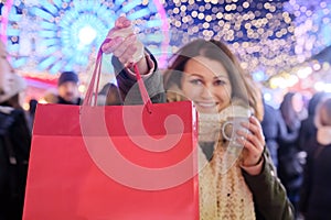 Happy woman shows red Christmas shopping bags, focus on the bag, place for text