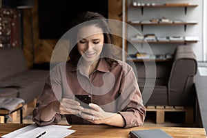 Happy woman sit at desk use cellphone text online