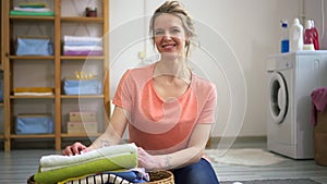 Happy woman sit on floor in laundry room do housework portrait. Spbd 30s smile joyful female folded