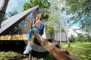 Happy woman sits on staircase with a cup of tea and enjoys fresh air and warm weather photo