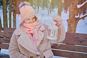 A happy woman is sitting on a bench with a lantern in her hands, a winter park with snow-covered trees