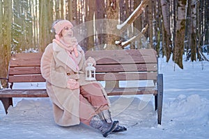 A happy woman is sitting on a bench with a lantern in her hands, a winter park with snow-covered trees