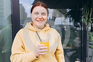 Happy woman sitting on the cafe terrace on the modern city street. 30s Person sitting at table and drinking drinks