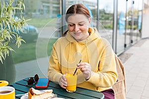 Happy woman sitting on the cafe terrace on the modern city street. 30s Person sitting at table and drinking drinks