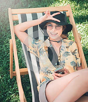 Happy woman sitting on a deck chair in a garden with hot summer sunshine