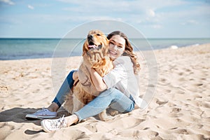 Happy woman sitting and hugging her dog on the beach