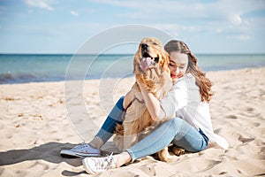 Happy woman sitting and hugging her dog on the beach