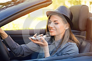 Happy woman sitting inside convertible car using a smart phone voice recognition function on line