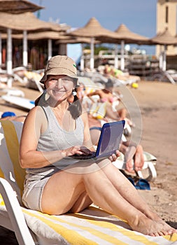 Happy woman sitting with laptop at beach