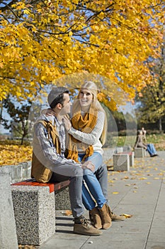 Happy woman sitting on man's lap at park during autumn