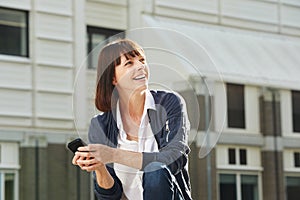 Happy woman sitting outside in city with smart phone