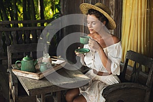 Happy woman sitting on the summer terrace and drinking coffee