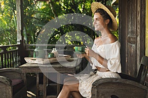 Happy woman sitting on the summer terrace and drinking coffee