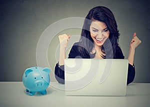 Happy woman sitting at table looking at laptop celebrates good news